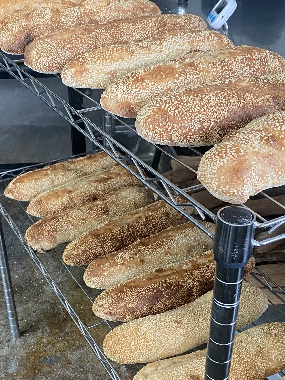 Freshly baked sesame-topped bread loaves cooling on racks in the Tackle Box dough lab.